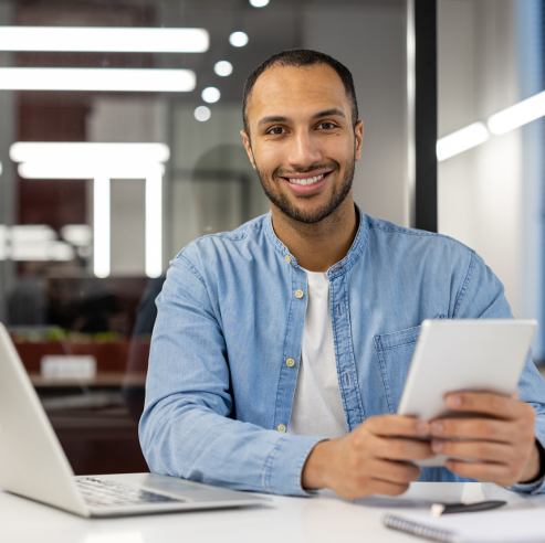 Mann mit Tablet in der Hand vor Laptop